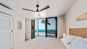 Quarto com cama grande, ventilador de teto, vista para a praia e porta de correr para o exterior.