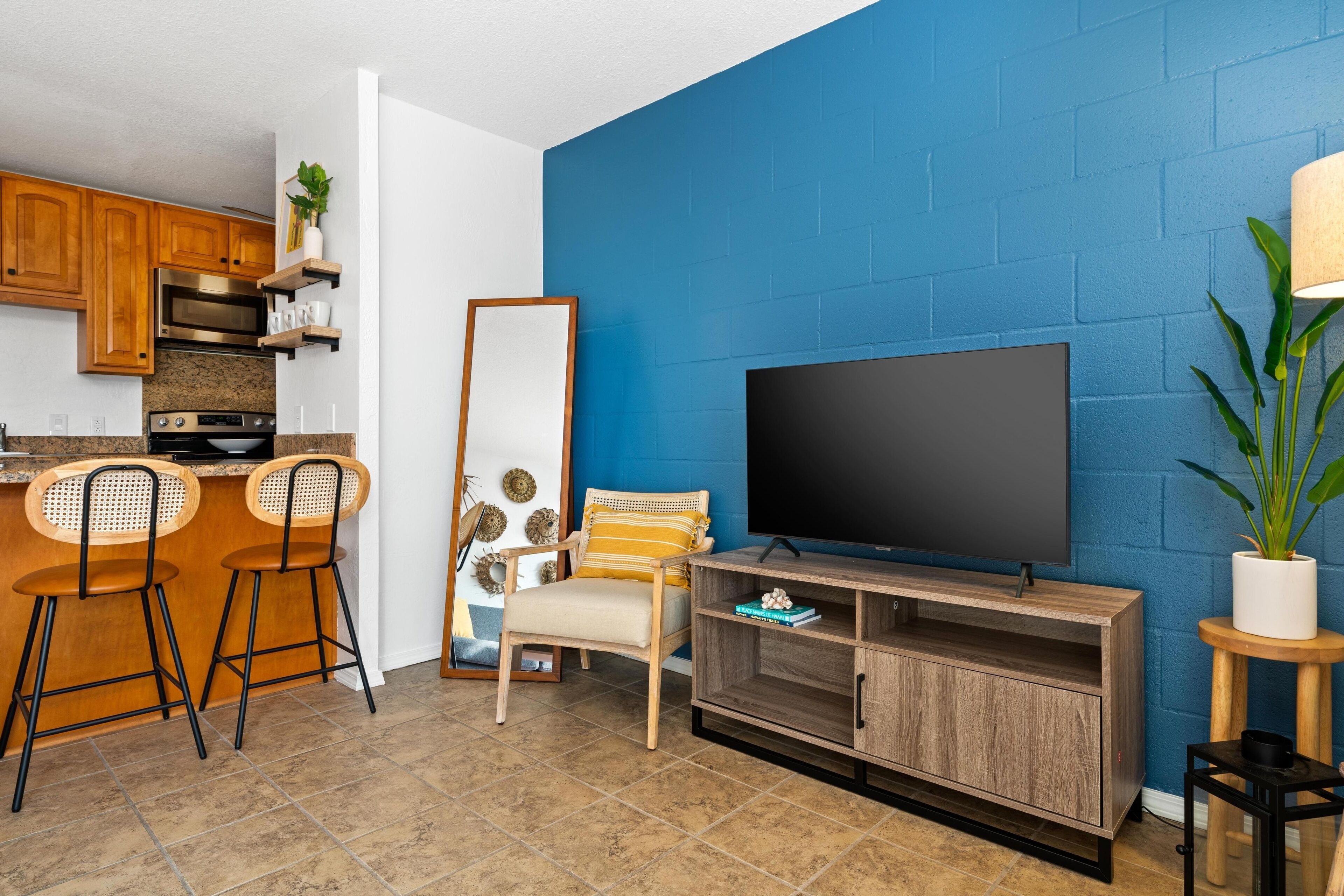 A compact living space with a kitchen, a dining area with bar stools, a TV, and a blue accent wall.
