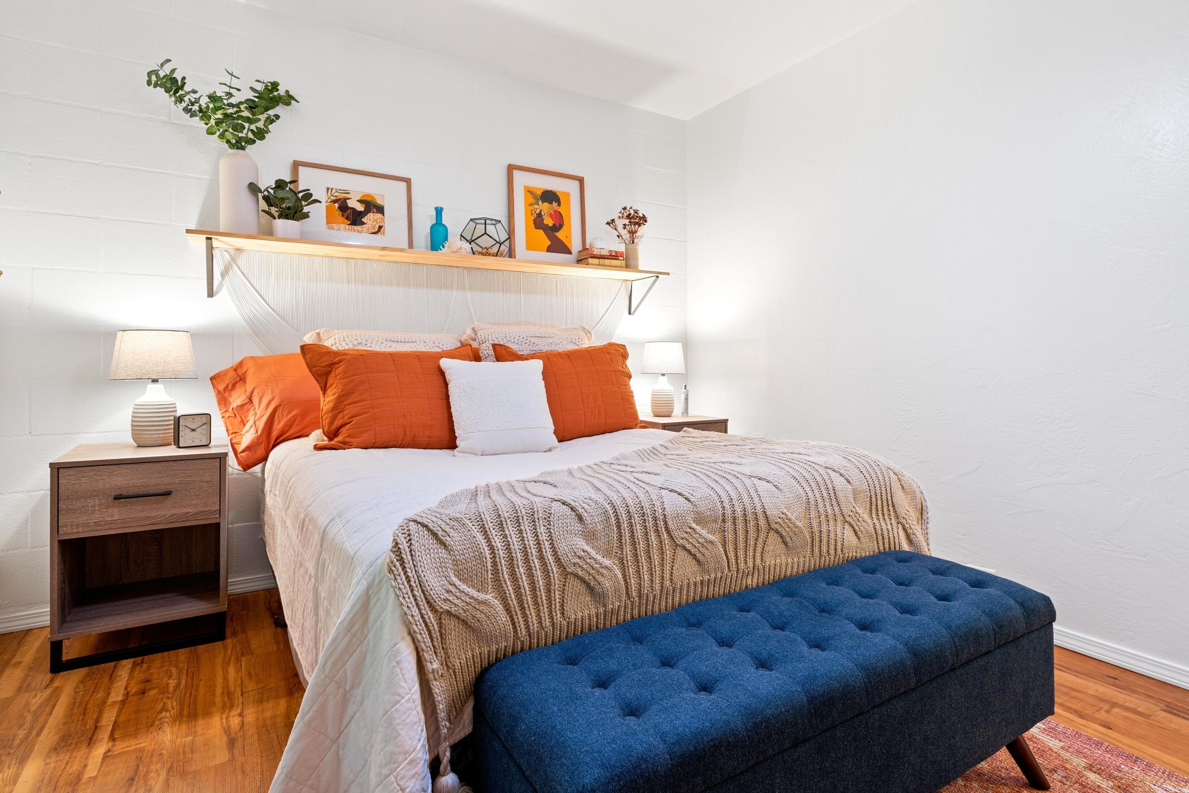A neatly arranged bedroom with a bed, bedside tables, a bench, and a shelf with decorative items.