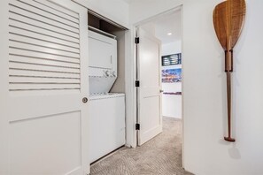 A hallway with a white door, a wooden paddle on the wall, and a view of a cityscape through a window. - Wailea Elua, #0302 1 Bedroom Condo by RedAwning (Kihei)