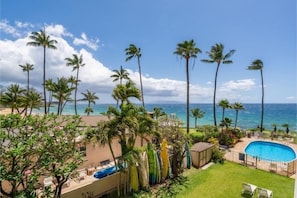 A pool area with a view of the ocean, surrounded by palm trees.