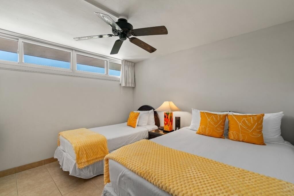 A hotel room with two beds, a ceiling fan, a nightstand with a lamp, and a window with curtains.