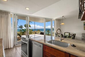 A kitchen with a view of the ocean, a dishwasher, and a dining area with chairs. - Kamaole Nalu, #303 2 Bedroom Condo by RedAwning (Kihei)