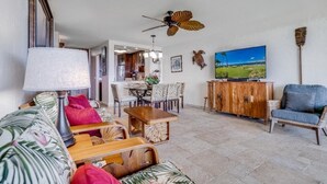A living room with a sofa, coffee table, and chairs, a wooden cabinet, a ceiling fan, and a painting on the wall. - Menehune Shores, #115^ 3 Bedroom Condo by RedAwning (Kihei)