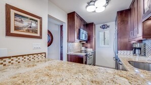 A kitchen with granite countertops, dark wooden cabinets, a microwave, and a coffee maker.