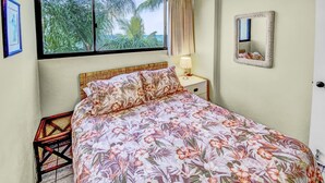 Un dormitorio con cama, mesita de noche, lámpara, ventilador de techo, ventana con cortinas y espejo.