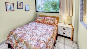 A bedroom with a bed, a nightstand, a lamp, a ceiling fan, and framed pictures on the wall.