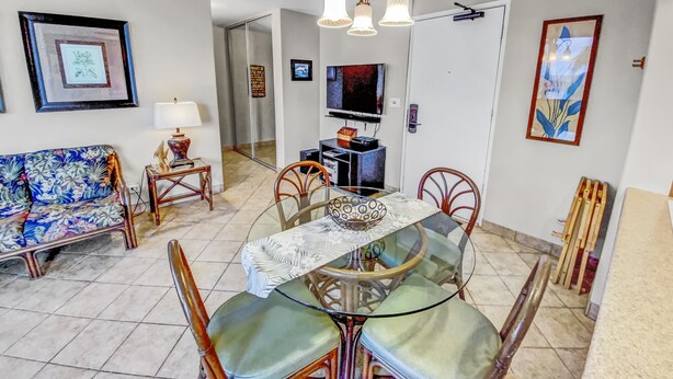 A dining area with a glass table and chairs, a sofa, a television, and a chandelier.