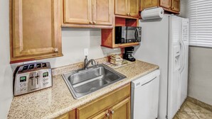 Una cocina con armarios de madera, un lavamanos de acero inoxidable, una cafetera y un lavavajillas blanco.