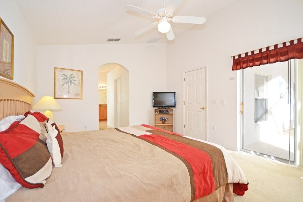 A bedroom with a bed, a ceiling fan, a TV, and a sliding glass door.