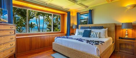 Een slaapkamer met een groot raam, met uitzicht op palmbomen en de oceaan.