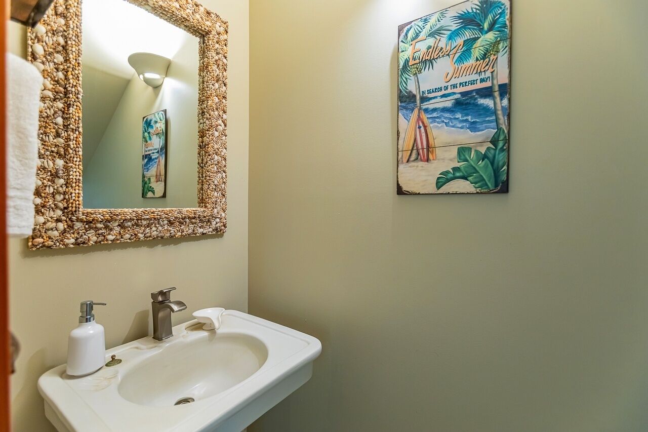 A bathroom with a white sink, a mirror with a textured frame, and a beach-themed poster on the wall.