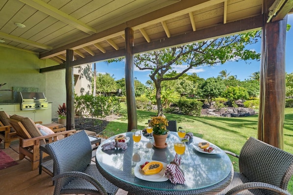 Une terrasse extérieure avec une table ronde en verre, des chaises en osier et un barbecue.