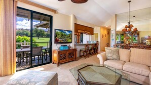 A spacious living area with a large glass table, a sofa, and a dining area with wooden chairs.