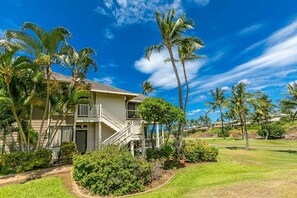 A two-story house with a balcony, surrounded by palm trees and a well-maintained lawn.