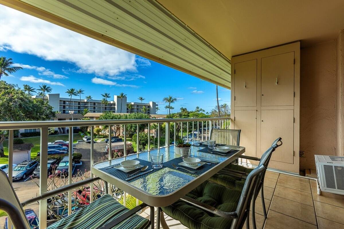 Ein Balkon mit einem Glastisch, grünen Sitzkissen und Blick auf einen Parkplatz und Gebäude.