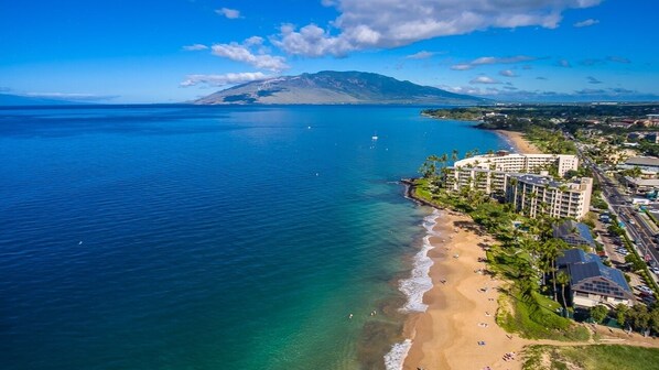 Ein Hotel an der Küste mit Blick auf den Strand, mehreren Etagen und einem markanten Berg im Hintergrund.