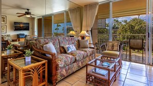 A spacious living area with a sofa, chairs, and a coffee table. There is a television on the wall and a ceiling fan. - Kihei Kai Nani by Coldwell Banker Island Vacations (Kihei)