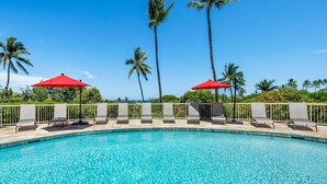 A swimming pool with lounge chairs and red umbrellas, surrounded by palm trees. - Big Island Keauhou Akahi #311 1 Bedroom Home (Kailua-Kona)
