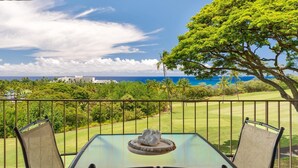 A table with chairs on a balcony overlooking a golf course and ocean. - Big Island Keauhou Akahi #311 1 Bedroom Home (Kailua-Kona)
