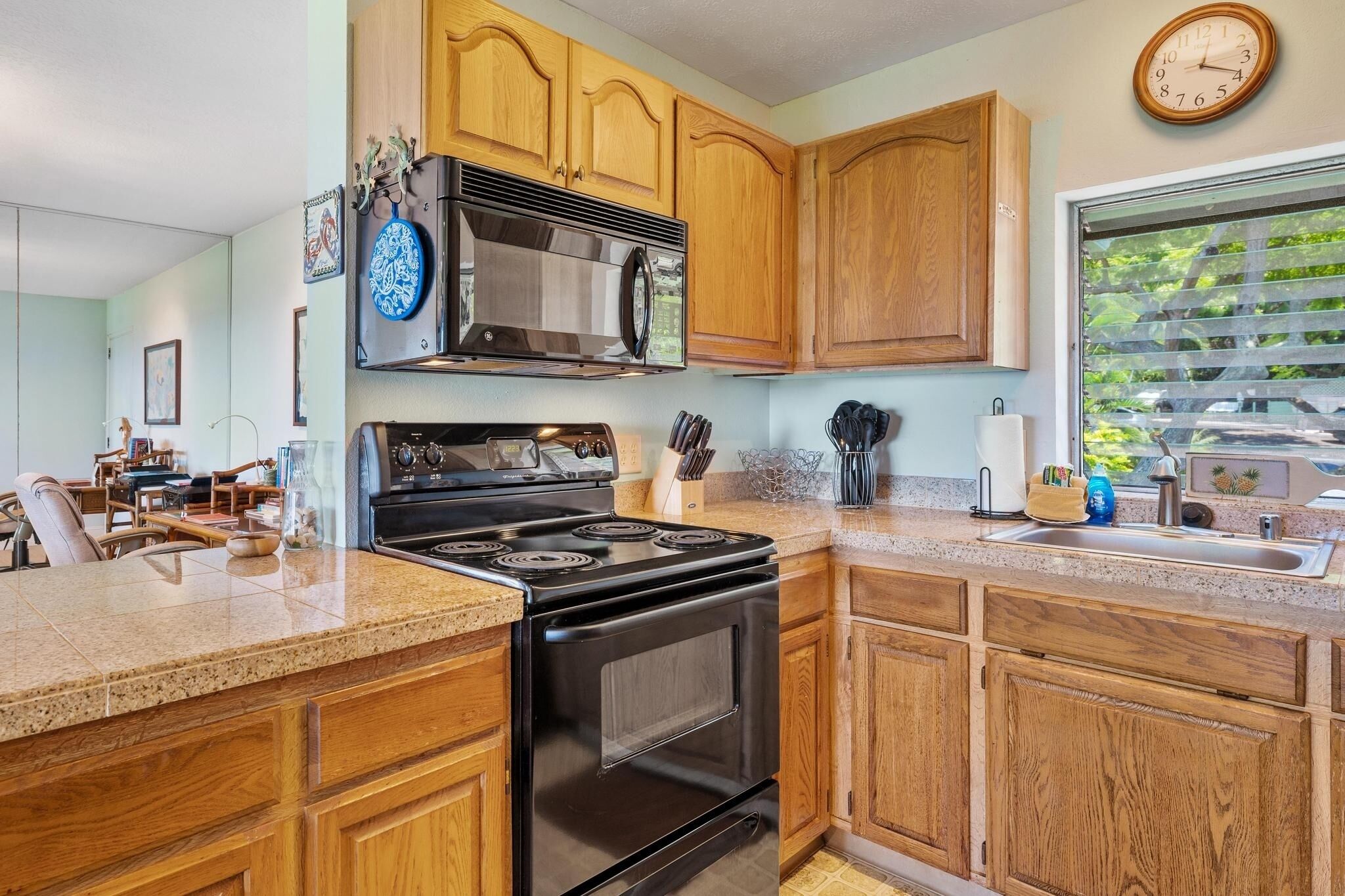 A kitchen with wooden cabinets, a black stove, a microwave, and a clock on the wall.