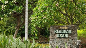 A stone sign with 'KEAUHOU AKAHI' and a number '78-7030' in a lush garden setting. - Big Island Keauhou Akahi #311 1 Bedroom Home (Kailua-Kona)