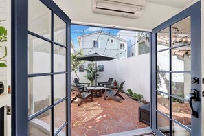 Eine offene Terrasse mit einem sechseckig gefliesten Boden, einem Tisch mit Stühlen und einem schwarzen Sonnenschirm.