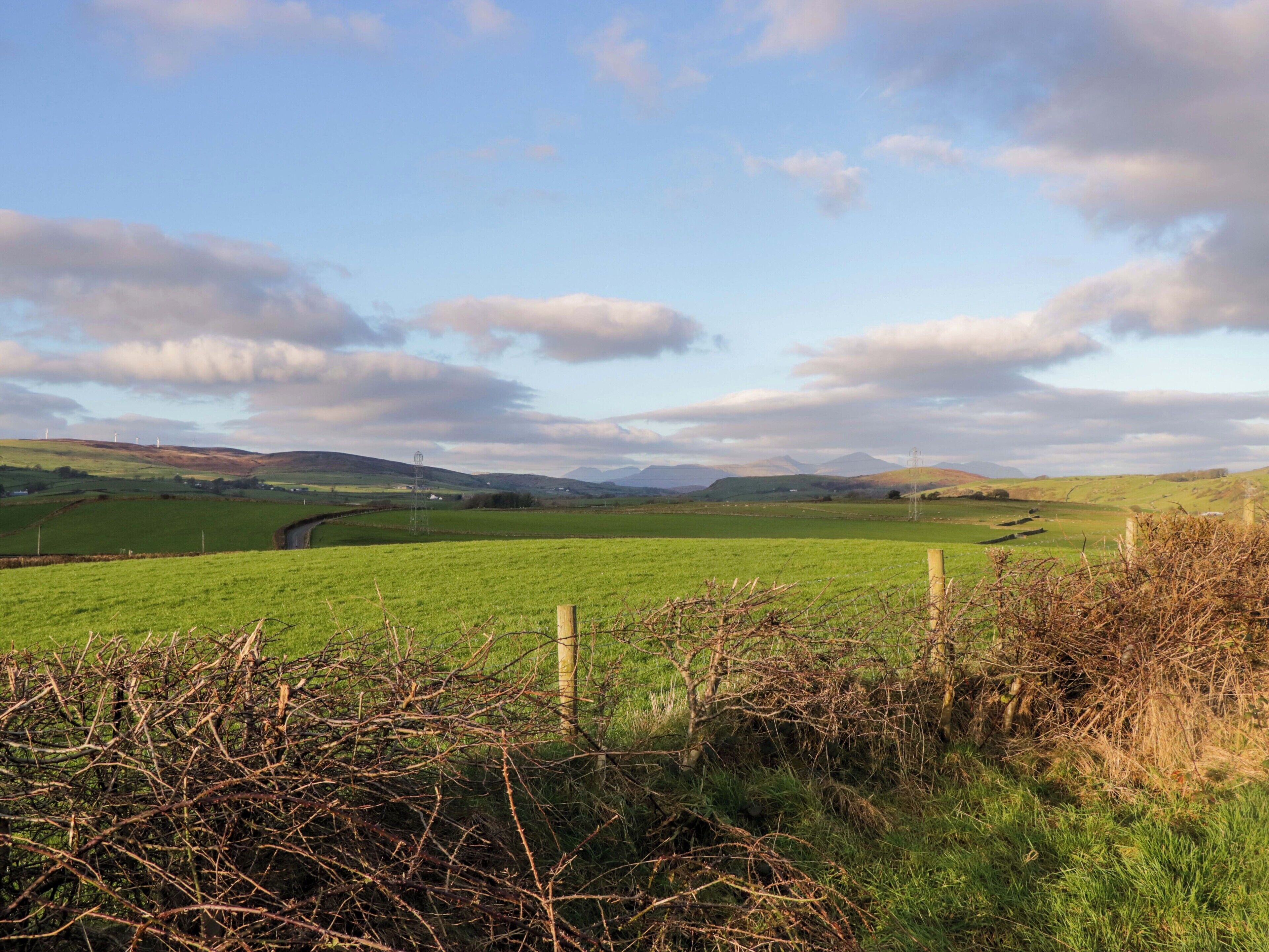 A rural landscape with rolling hills, a fence, and a clear sky.