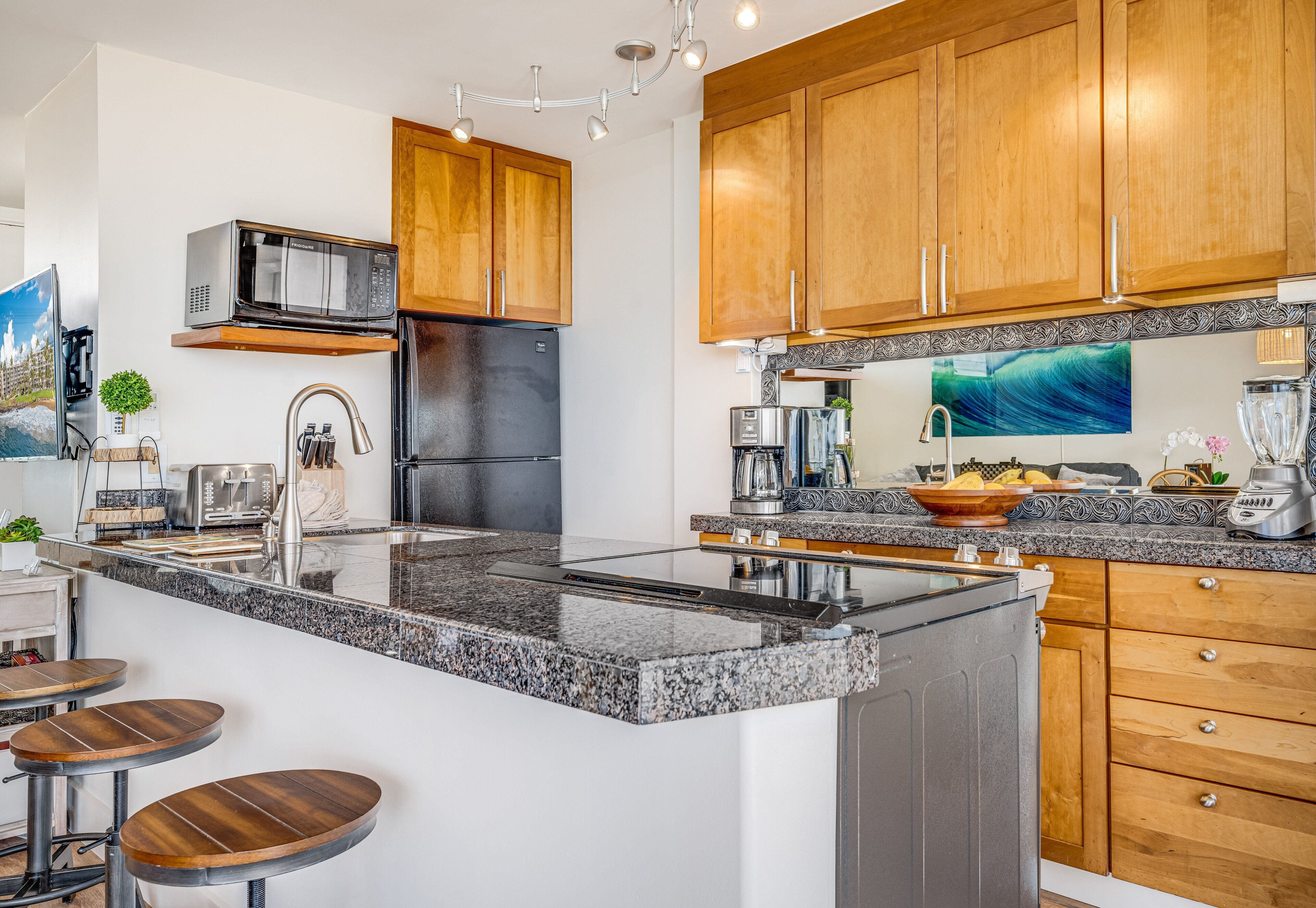 Een moderne keuken met granieten aanrechtbladen, roestvrijstalen apparatuur, houten keukenkastjes en een centraal eiland met barkrukken.