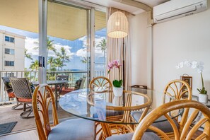 A round glass table with wicker chairs, a potted plant, and a view of palm trees and the ocean.