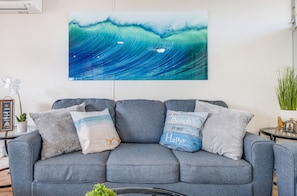A living room with a grey sofa, a framed picture of a wave, and decorative pillows.