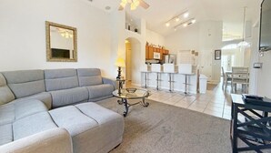 Een ruime woonkamer met een grijze modulaire bank, een glazen salontafel en een plafondventilator.