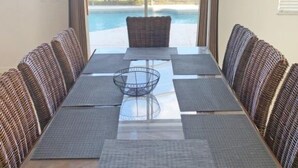 Een eetgedeelte met een lange tafel, rieten stoelen en uitzicht op een zwembad.
