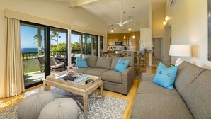 A spacious living area with a large sofa set, a coffee table, and a view of the ocean through large sliding doors.