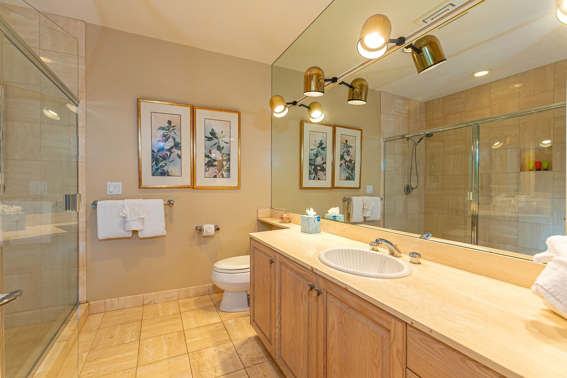 Un bagno moderno con cabina doccia in vetro, mobile bagno in legno con lavello e opere d'arte incorniciate a parete.