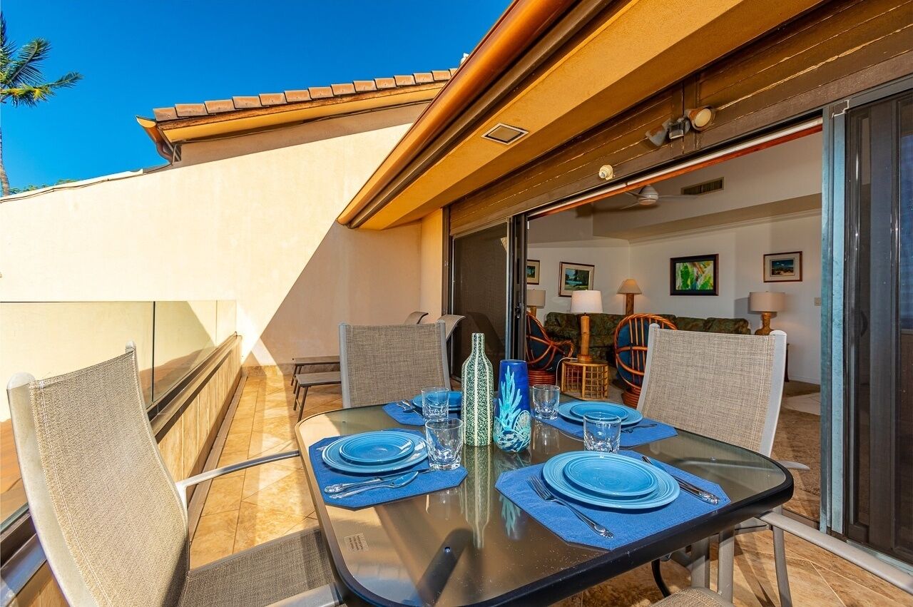 A dining area with a glass table set for four, surrounded by chairs, with a view of the interior through glass doors.