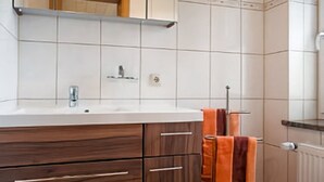 Une salle de bain avec un mur recouvert de carreaux blancs, un meuble-lavabo en bois avec un miroir, un évier et un porte-serviettes.