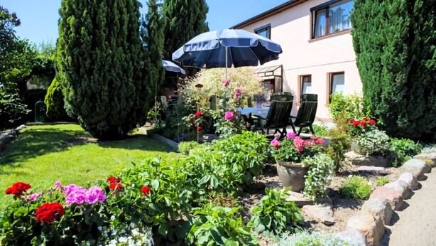 Un jardin bien entretenu, agrémenté d’une terrasse, d’une table avec des chaises et d’un grand parasol offrant de l’ombre.