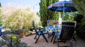 Une terrasse extérieure avec une table et des chaises, entourée d’une végétation luxuriante et de plantes en fleurs.