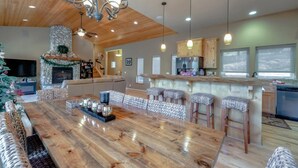 Amplia sala de estar con una mesa de comedor de madera, chimenea y una cocina con taburetes de bar.
