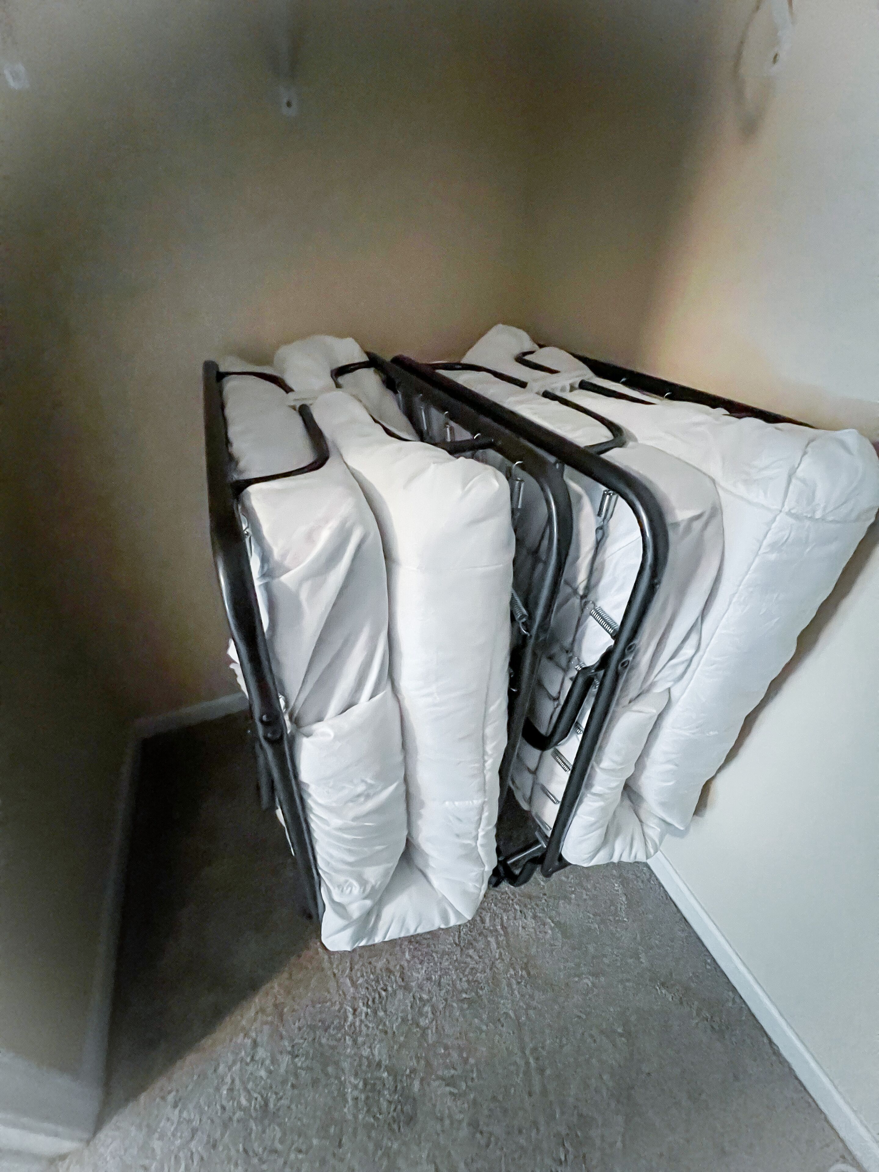 A corner of a room with a corner shelf holding several white pillows and a black metal frame.