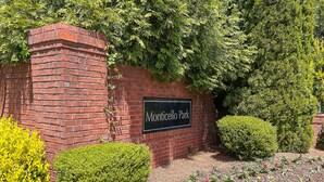 Un muro de ladrillo con un letrero que dice "Monticello Park" y un jardín bien cuidado con acolchado y arbustos.