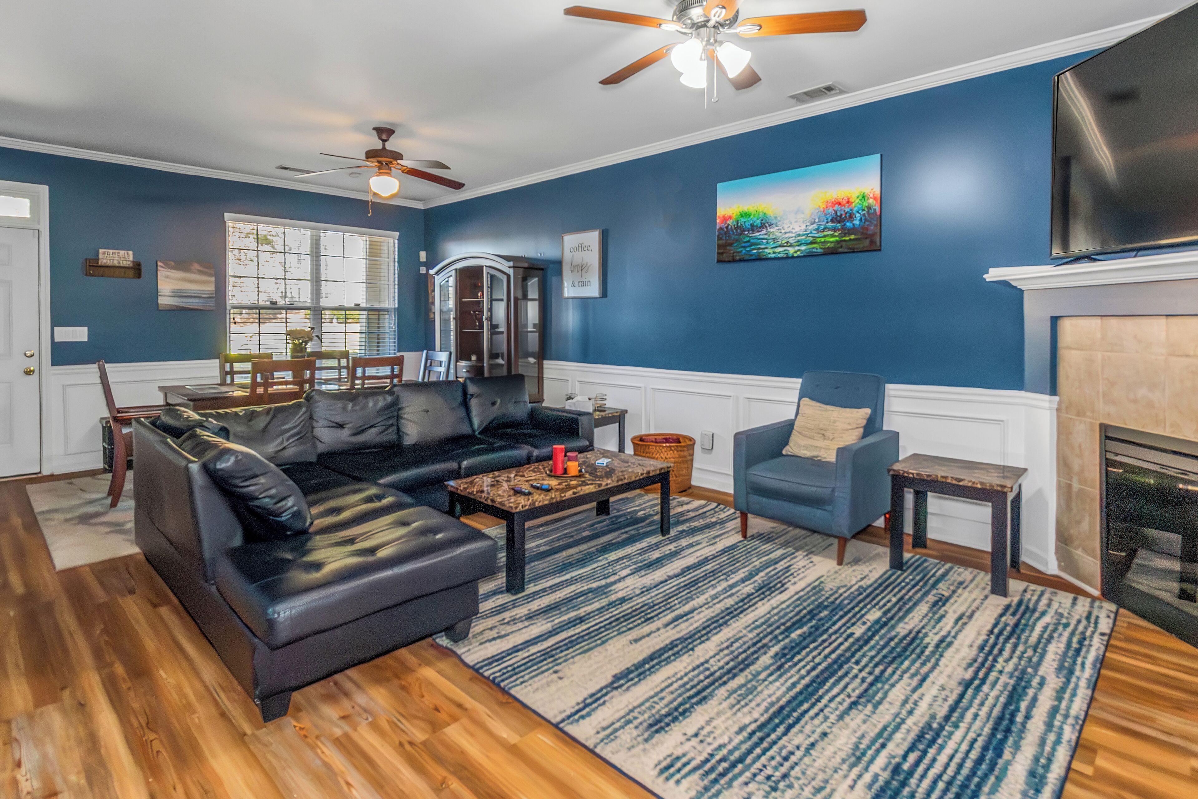 A living room with a sectional sofa, a blue armchair, a fireplace, and a ceiling fan.
