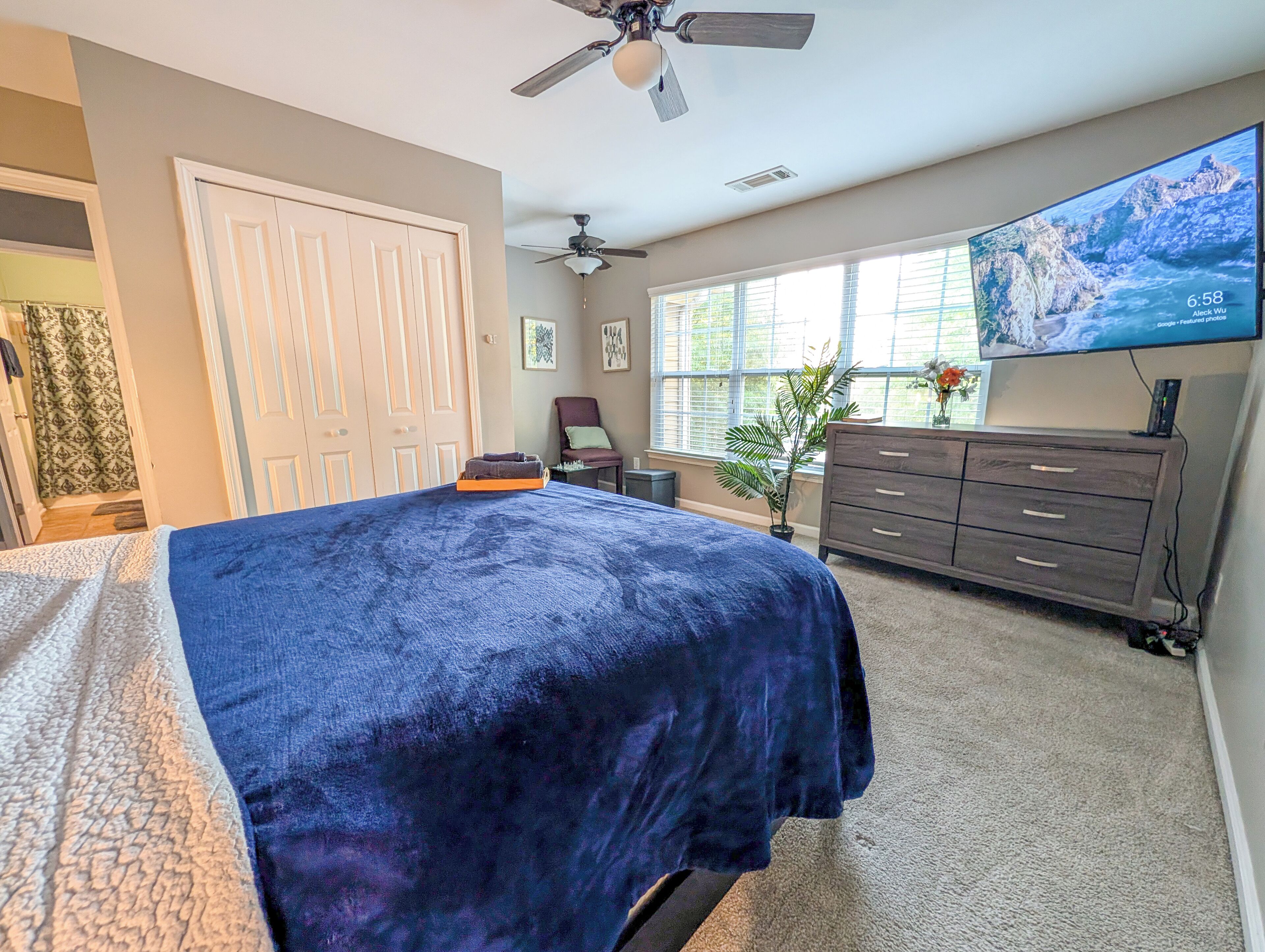 A bedroom with a bed, a ceiling fan, a TV, a dresser, and a window.