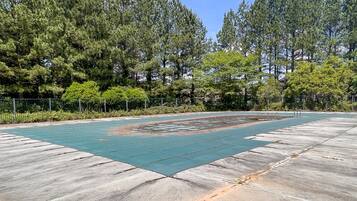 A concrete outdoor area with a green rubberized surface, surrounded by trees and a metal fence.