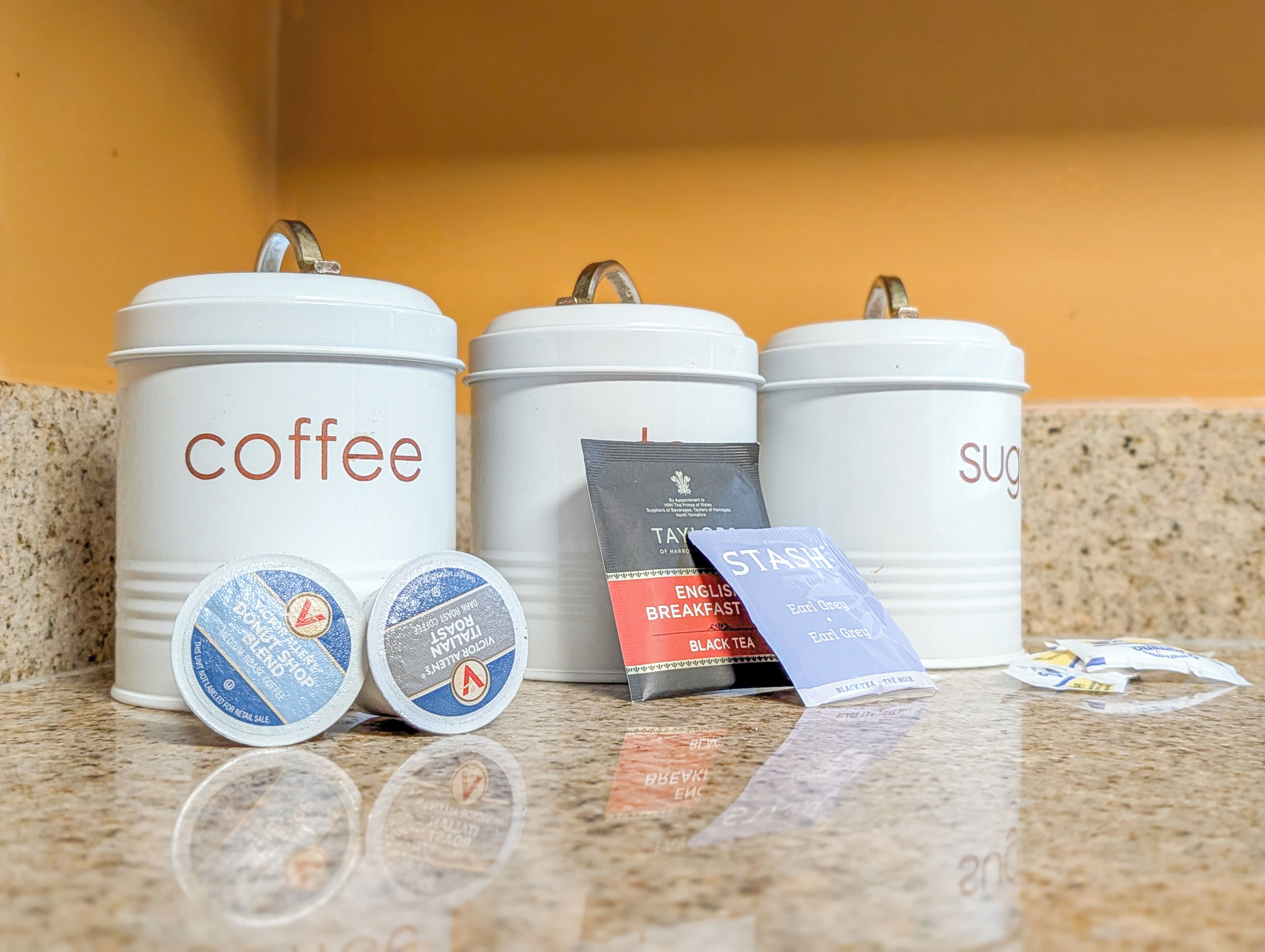Three white containers labeled 'coffee,' 'black tea,' and 'sugar' on a countertop.