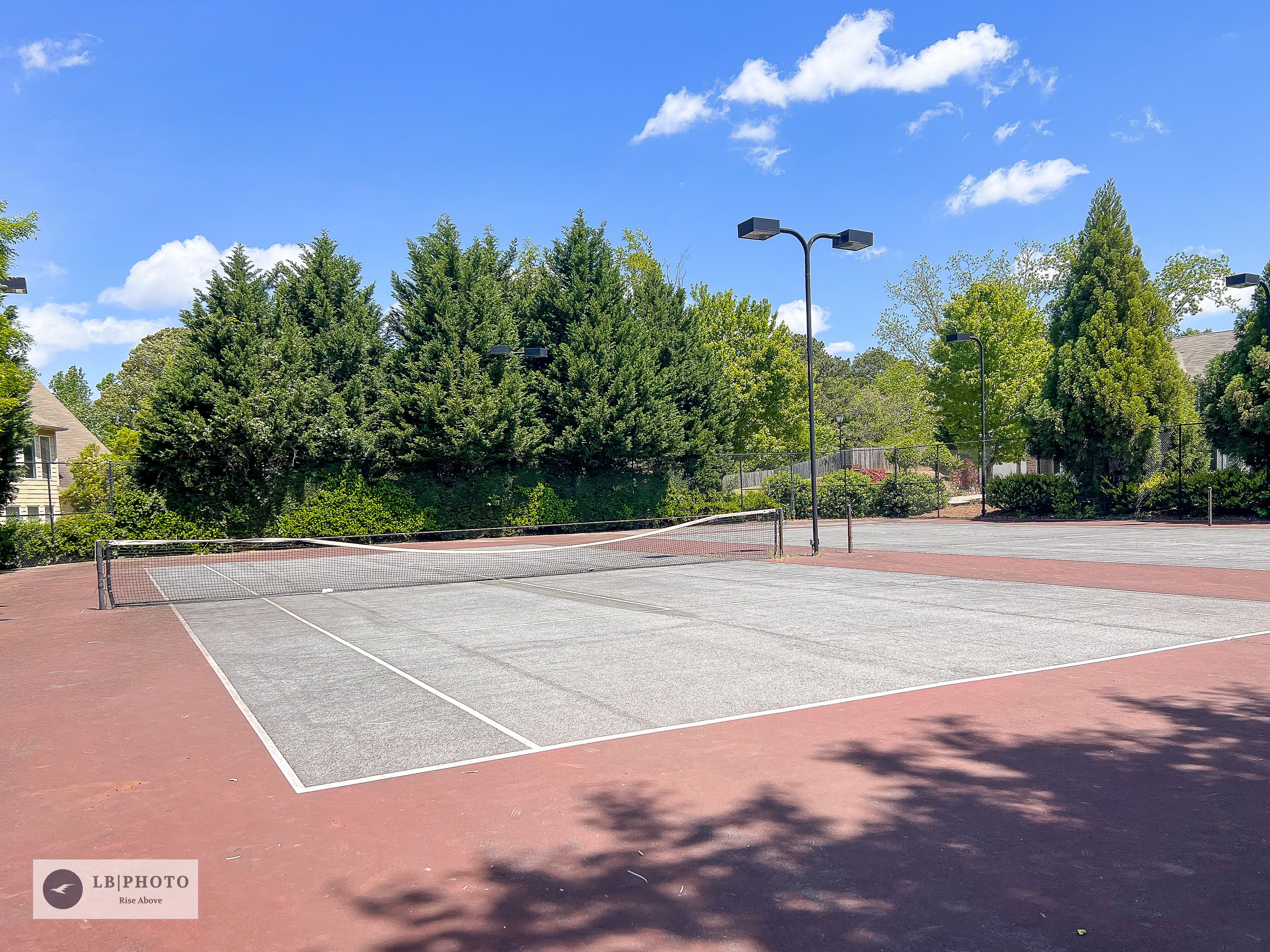 Cancha de tenis al aire libre con red, rodeada de árboles y un cielo despejado.