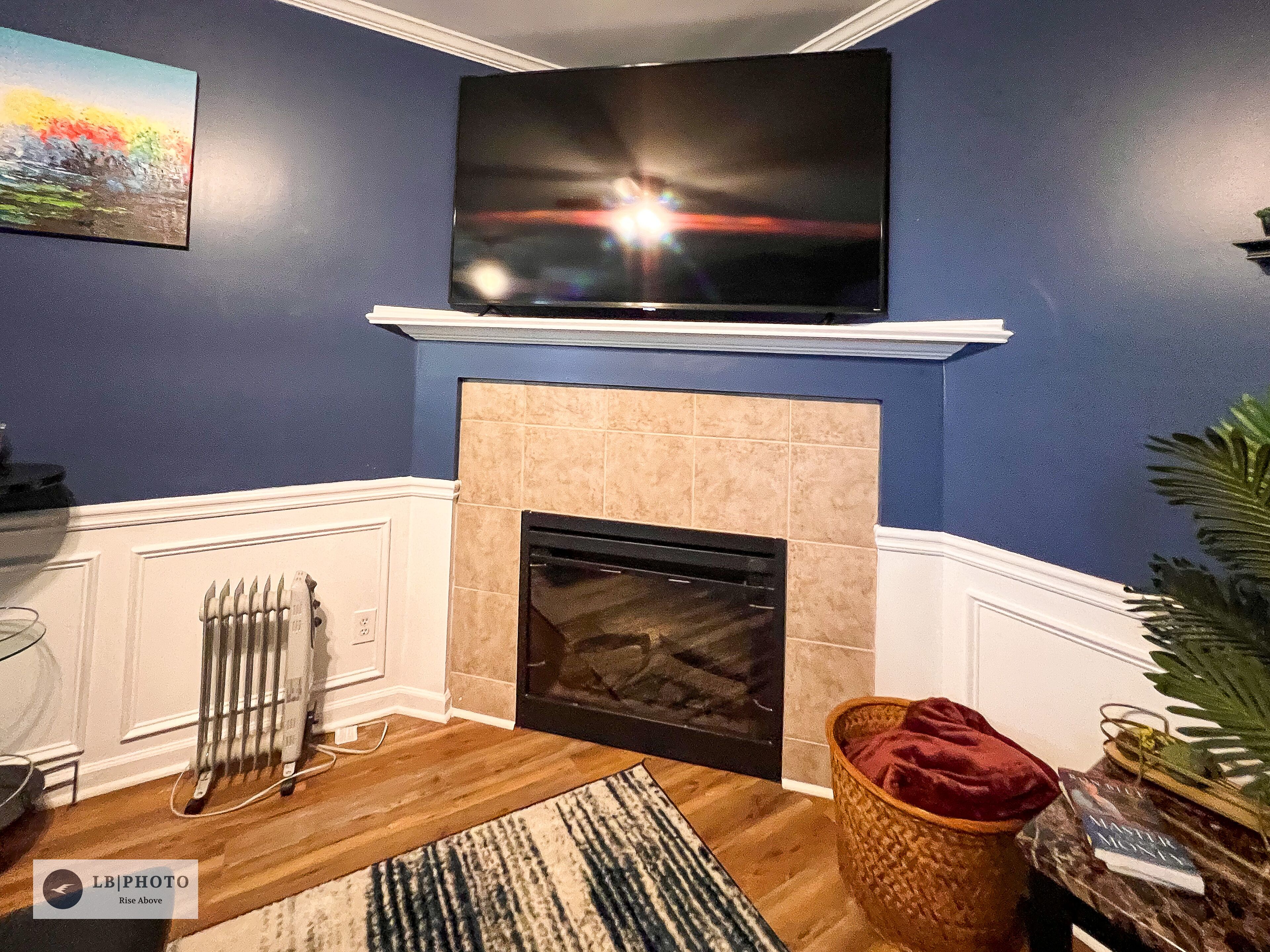 A living room with a fireplace, a television mounted above it, and a painting on the wall.