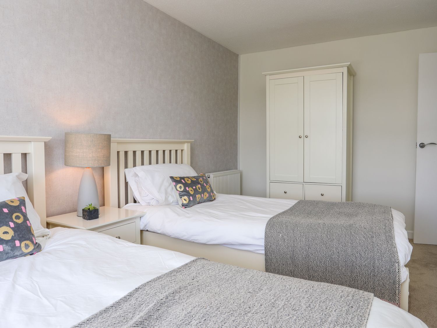 A bedroom with two beds, a wardrobe, and a nightstand with a lamp.