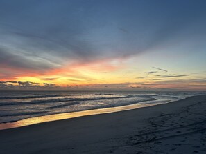 Une plage au coucher du soleil, avec des vagues et des empreintes de pas dans le sable.